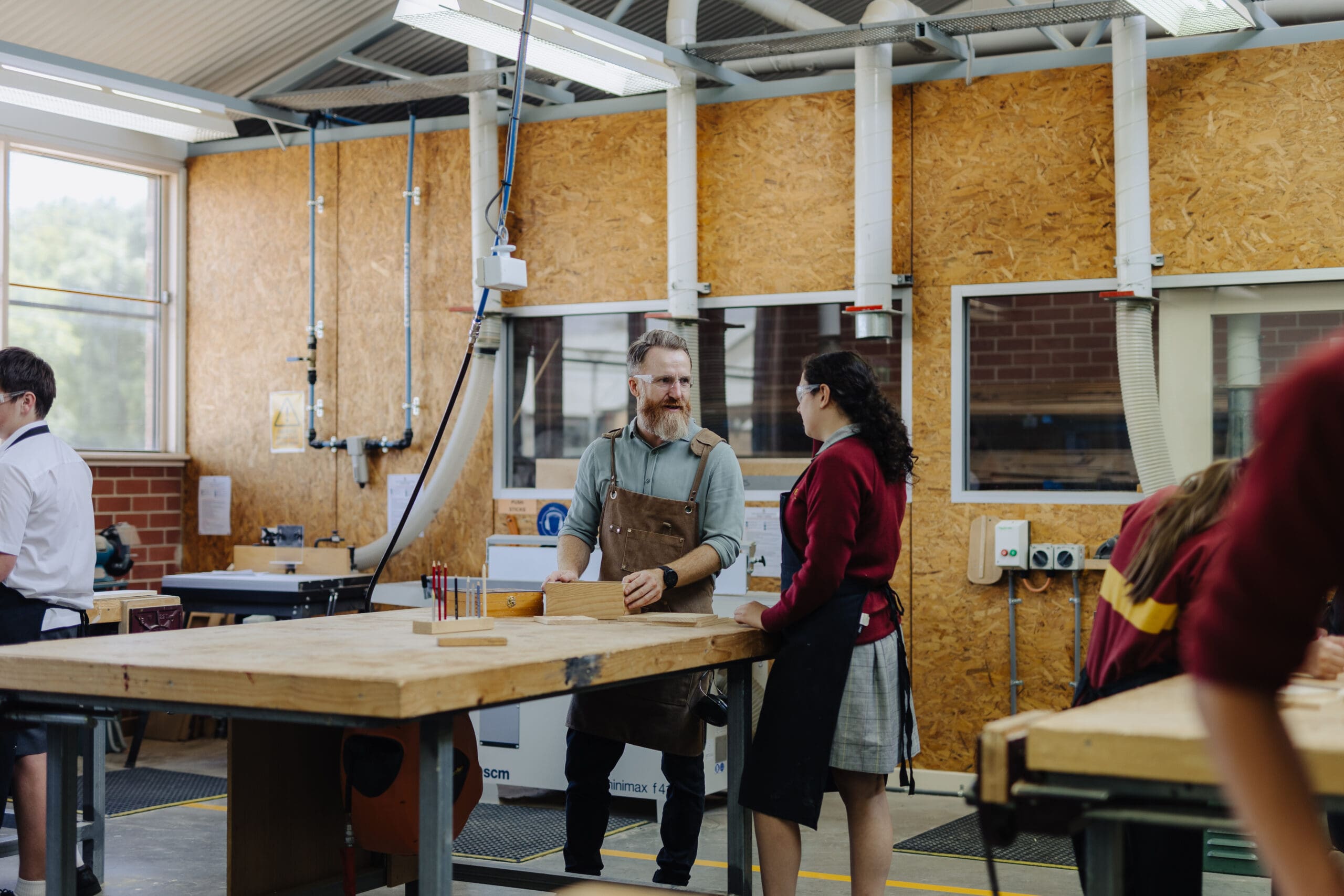 A design and technology teacher helps student with measuring a timber block. 