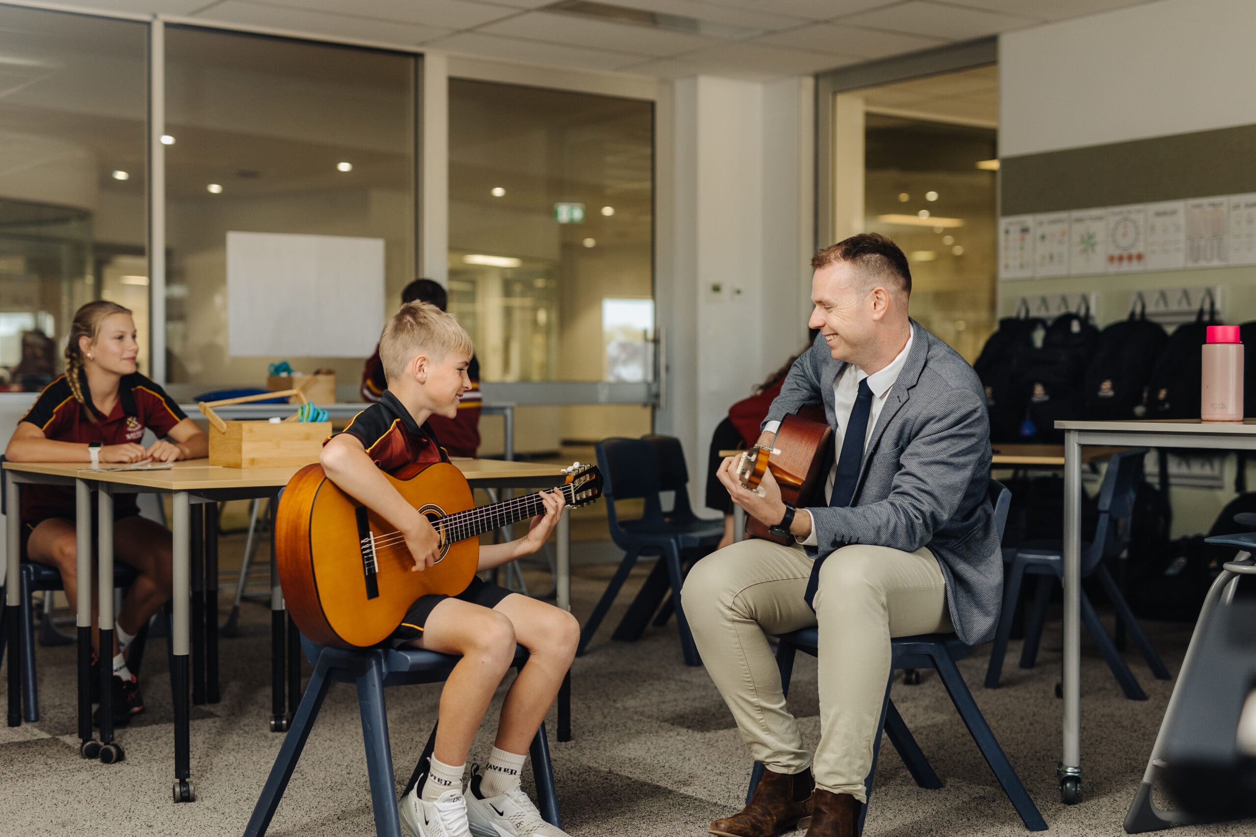 Music teacher showing a student how to play the guitar in a classroom. 