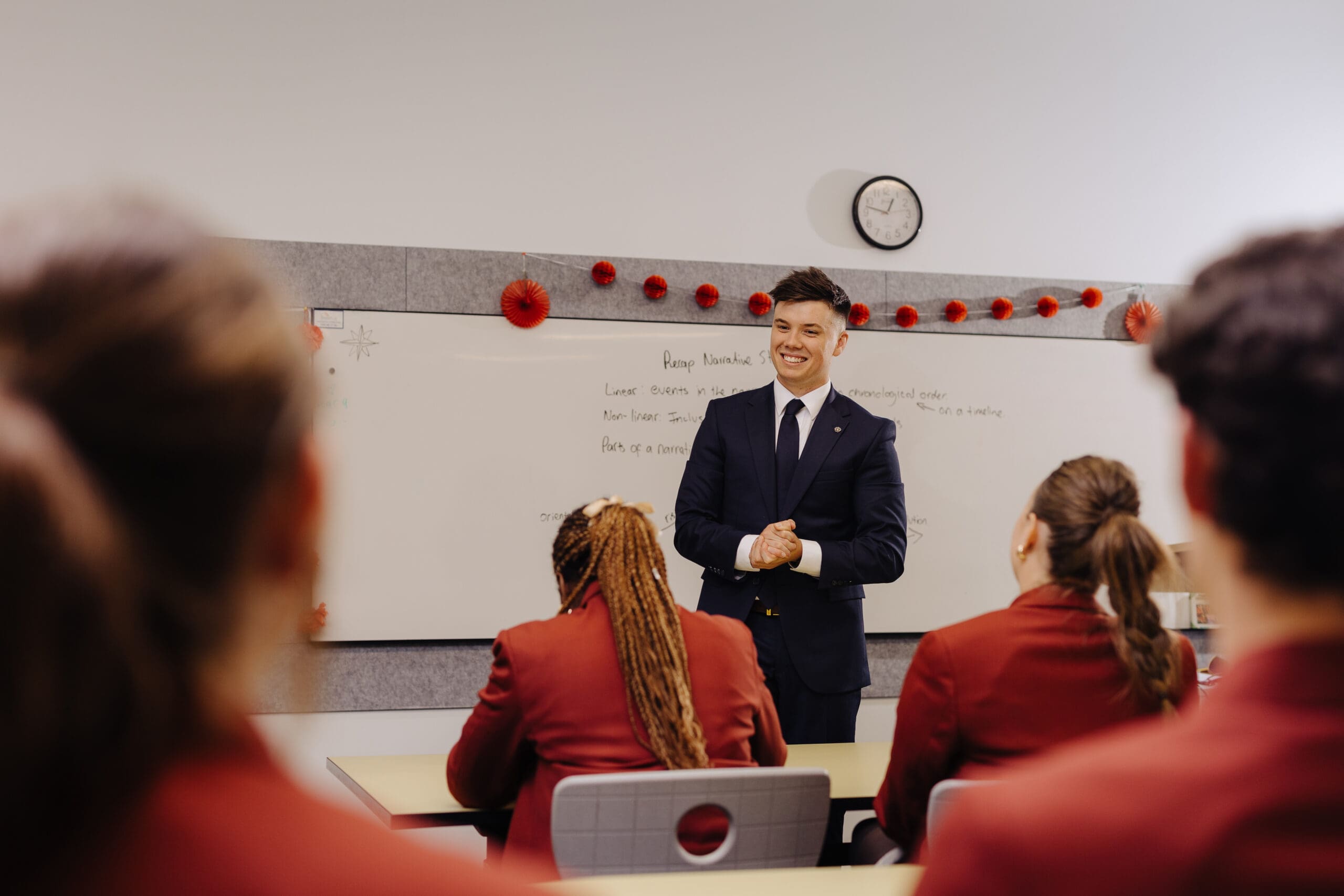 A young man pursuing his teaching career, standing at the front of a room of students.