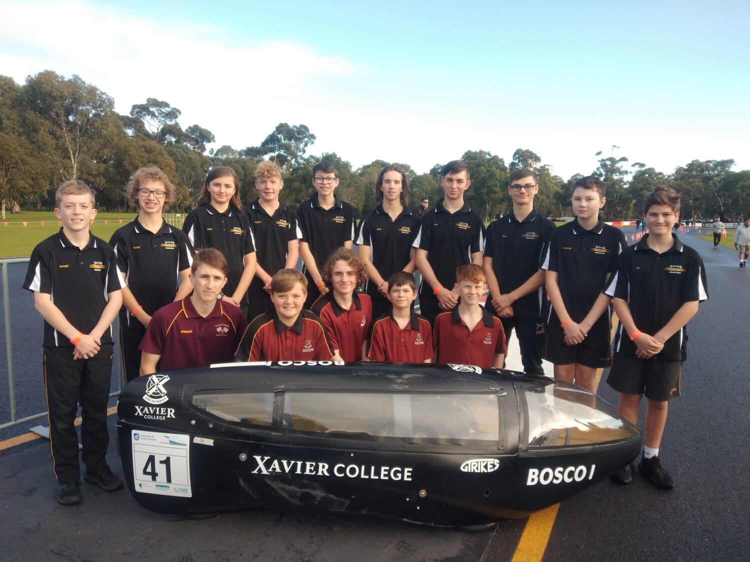 A team of students standing in two rows behind a human powered vehicle.