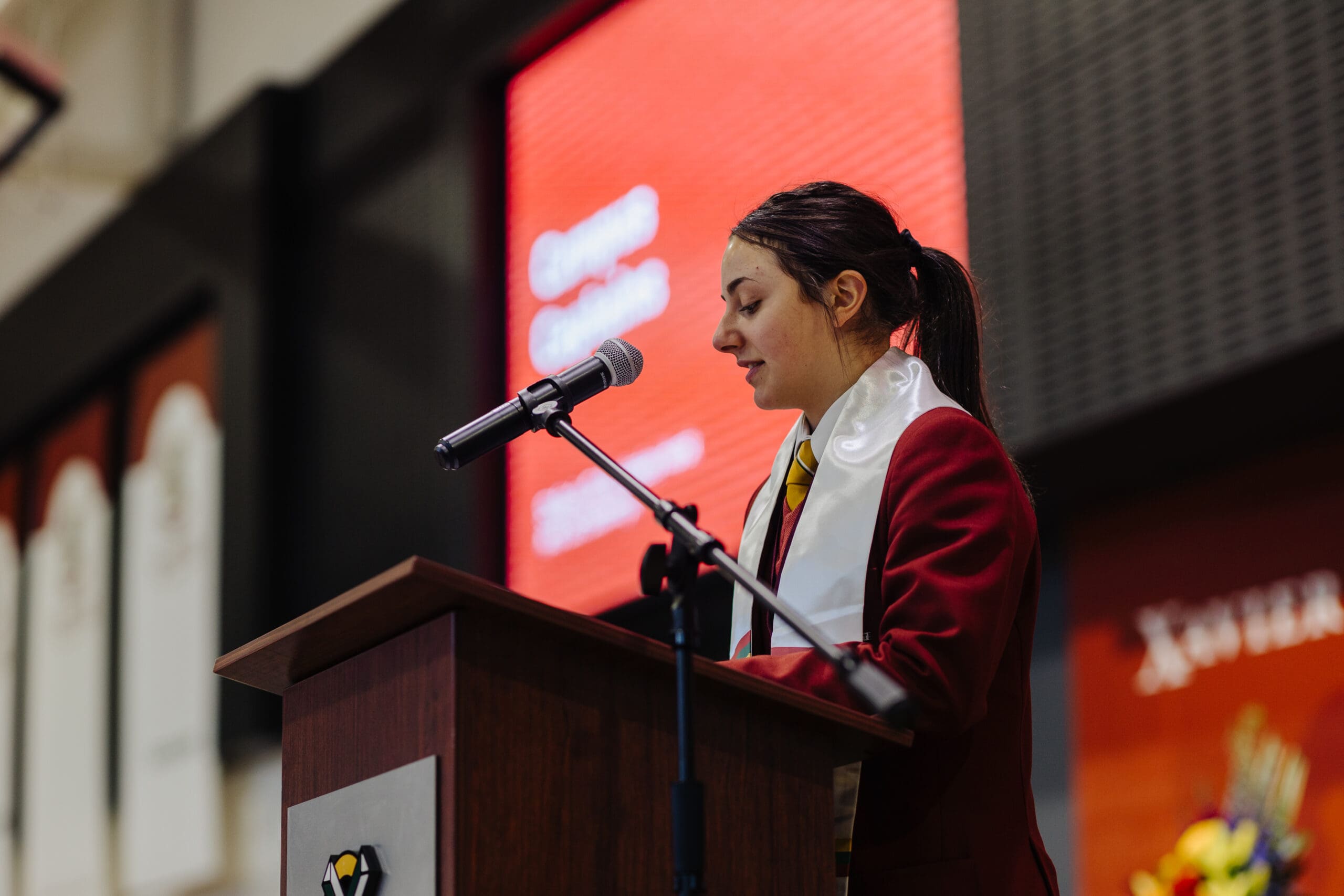 A female student leader at a podium speaking to an audience. 