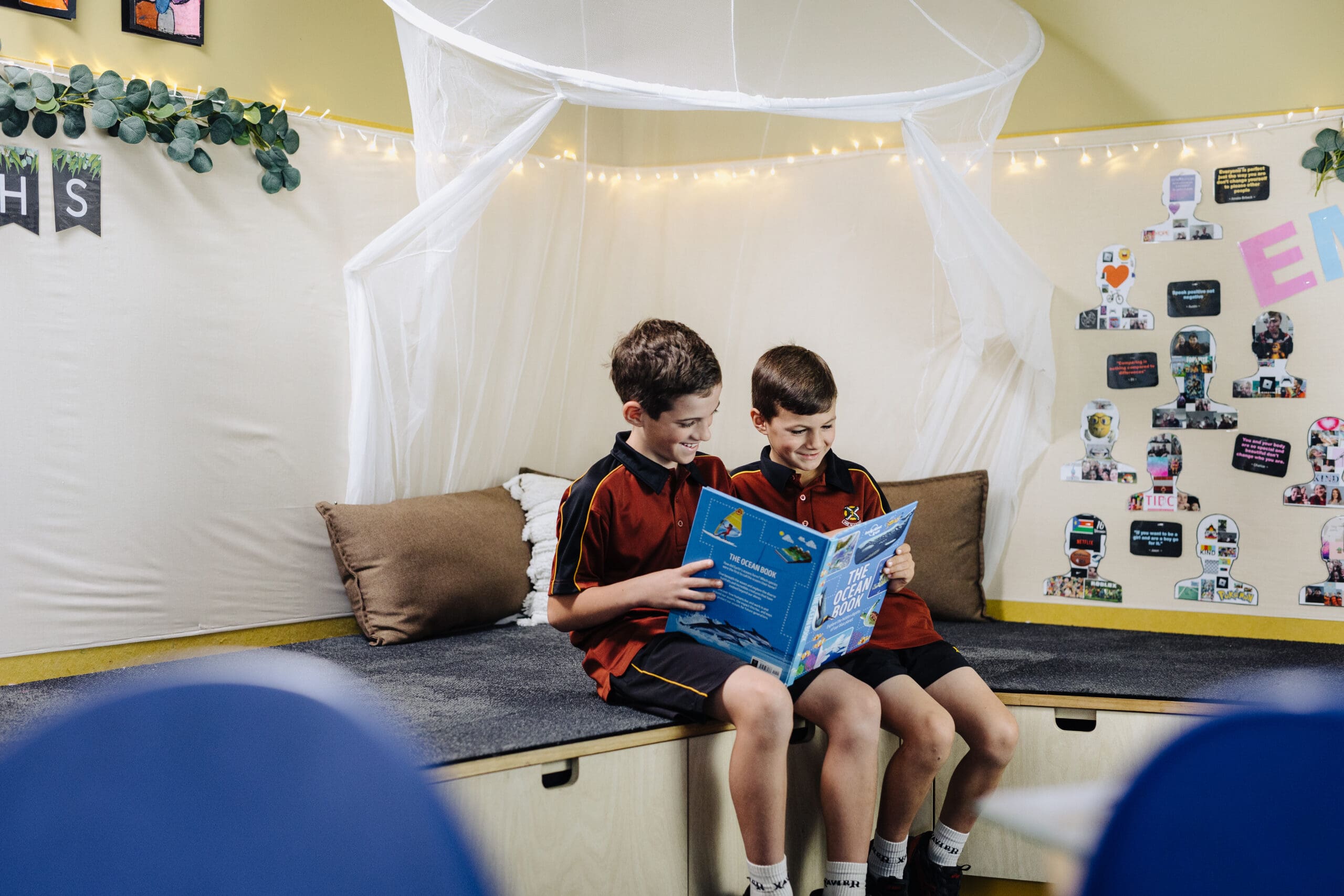 Primary years students reading a book togther in the corner of a classroom. 