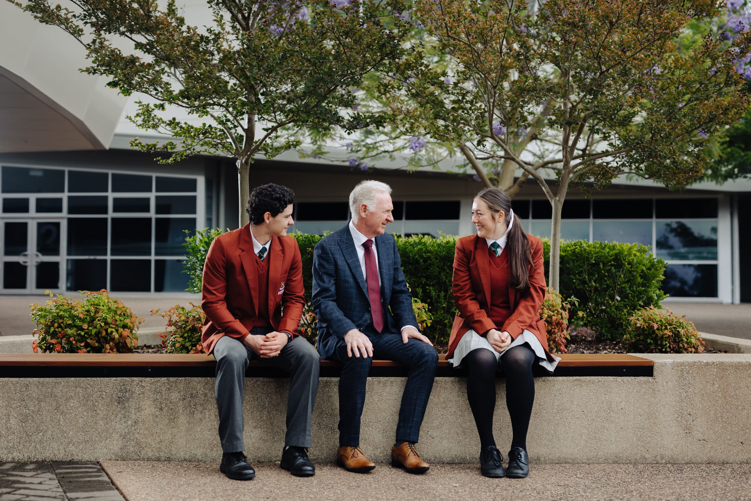 Principal Mark Flaherty sitting and conversing with two senior Xavier College students. 