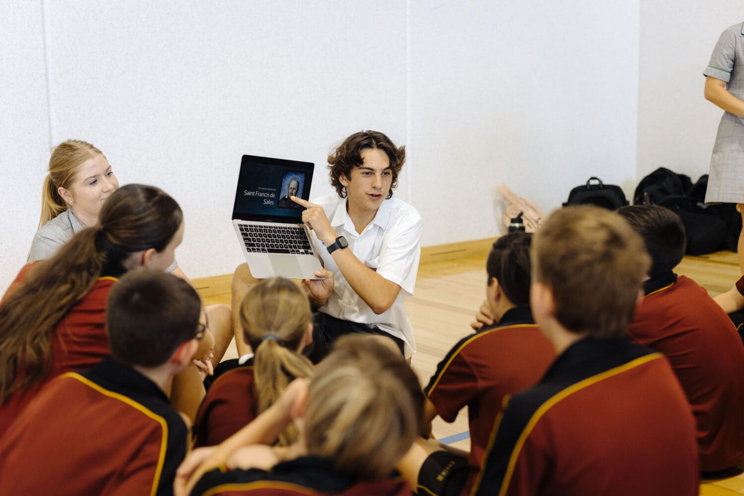 A male student leader giving an informative presentation to primary school students.